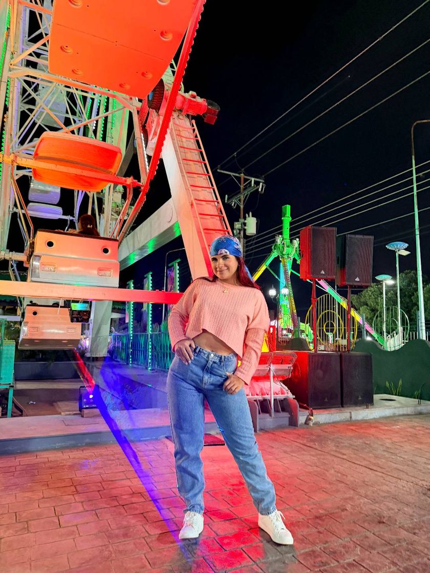 A woman at a fairground at night, with a big wheel lit up behind her